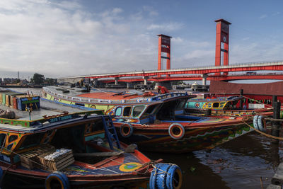 Fishing boats moored at harbor against sky in city