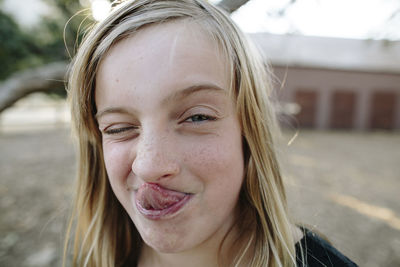 Close-up portrait of playful girl sticking out tongue while winking at farm