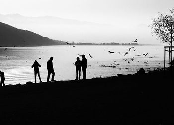 Silhouette people on beach against sky during sunset