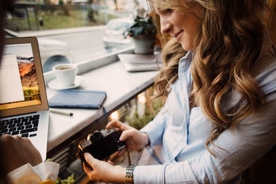 High angle view of young woman photographing with camera while sitting at cafe