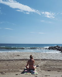 Woman sitting on beach by sea against sky
