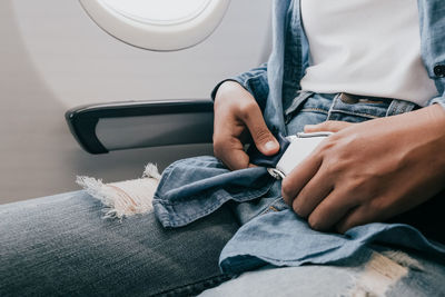 Midsection of man fastening seat belt in airplane