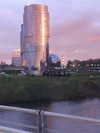 River by illuminated city against sky during sunset