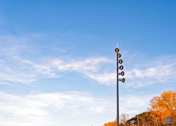 The led street light is set against a sky with clouds and trees with yellow foliage.