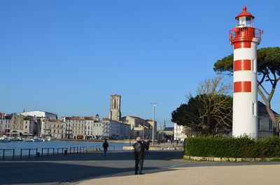 Low angle view of lighthouse by road against clear sky on sunny day