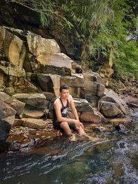 Full length of man sitting on rock by river