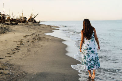 Rear view of woman standing on beach against clear sky