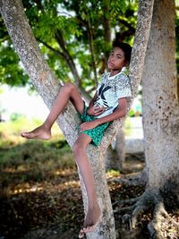 Full length of boy sitting on tree trunk