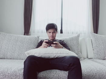 Young man using smart phone while relaxing on sofa at home