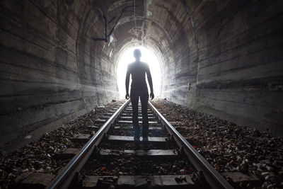 Rear view of woman standing on railroad track in tunnel