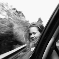 Portrait of smiling teenage girl with head outside window of car