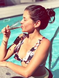 Woman drinking while standing in swimming pool during sunny day