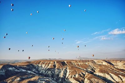 Hot air balloons flying against blue sky over rocks