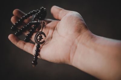 Close-up of hand holding beads against black background