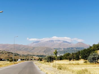 Road leading towards mountains against blue sky