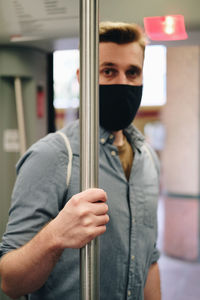 Portrait of man wearing mask holding metallic pole in train