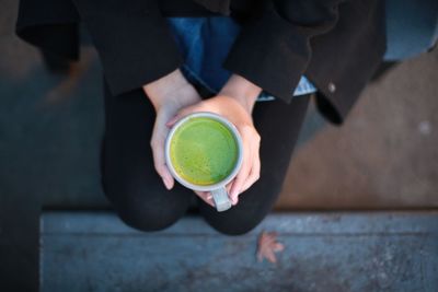Midsection of woman holding matcha tea while sitting outdoors