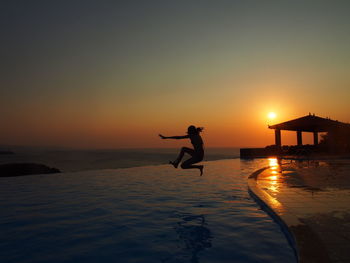 Silhouette man standing in sea against sky during sunset