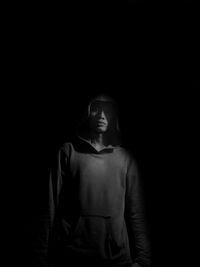 Portrait of young man wearing hooded shirt standing against black background