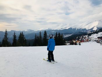 Rear view of mid adult woman skiing on snowcapped mountain against cloudy sky