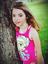 Portrait of smiling young woman standing against tree trunk