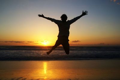 Silhouette woman jumping on beach against sky during sunset