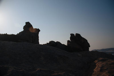 Silhouette man relaxing on rock against clear sky