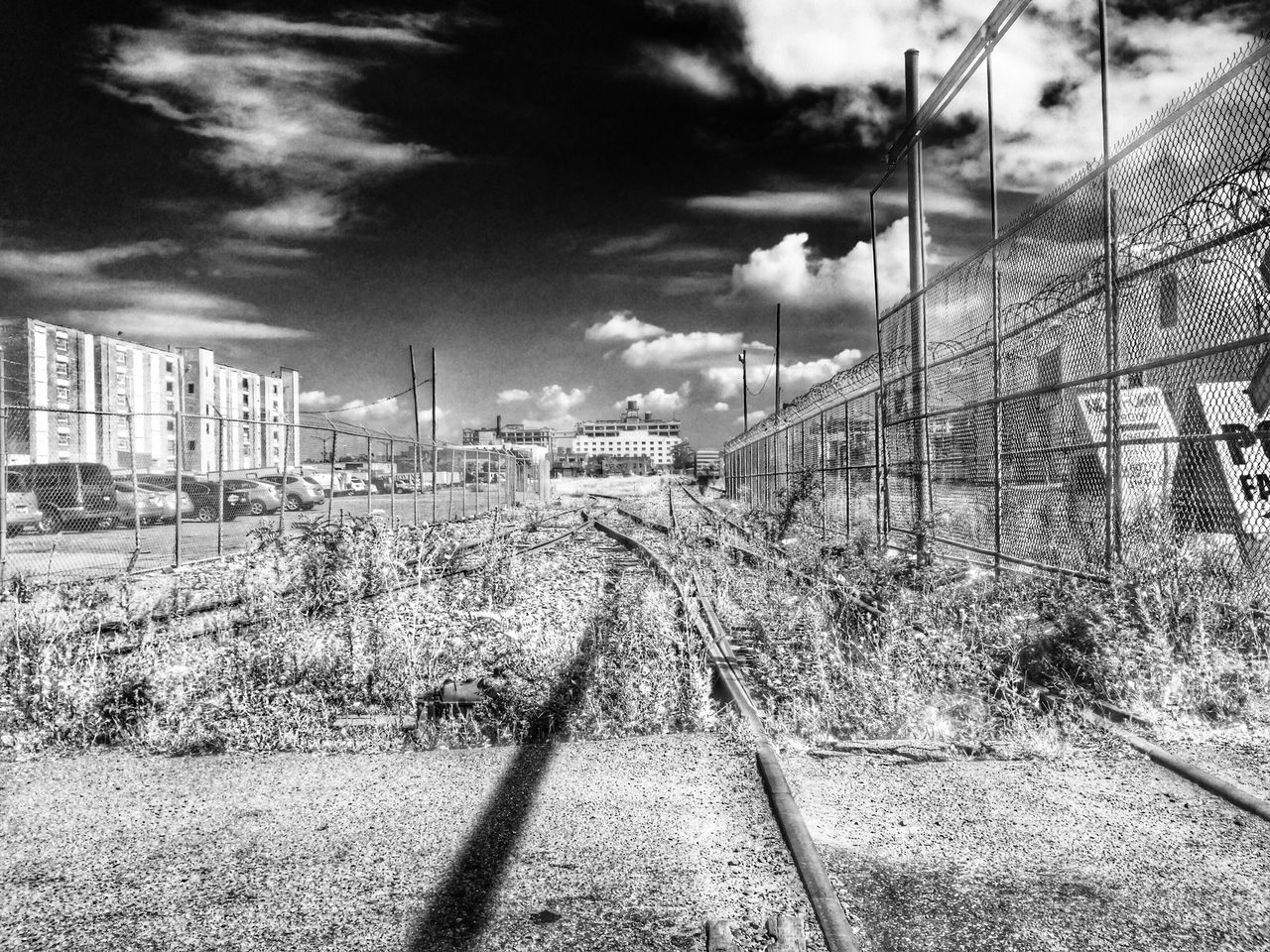 building exterior, architecture, built structure, the way forward, sky, transportation, city, diminishing perspective, railroad track, vanishing point, street, cloud - sky, road, day, sunlight, outdoors, tree, residential structure, no people, high angle view