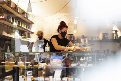 Busy baristas in protective masks making delicious coffee while standing at counter in cozy coffee house during coronavirus pandemic