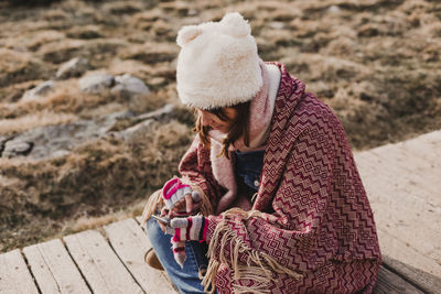 High angle view of woman using mobile phone while sitting on footpath during winter