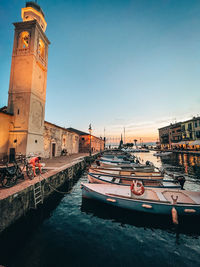 Boats moored in canal by buildings against sky during sunset