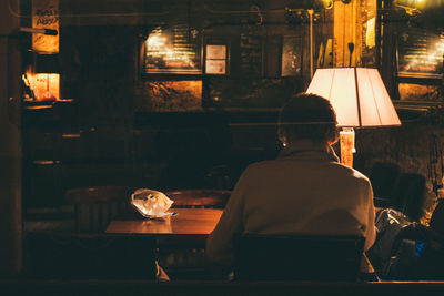 Rear view of woman sitting in illuminated building