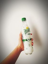 Human hand holding bottle against wall