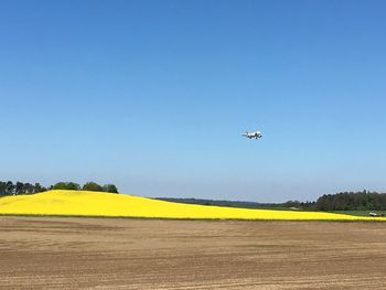 Airplane flying over field against clear blue sky