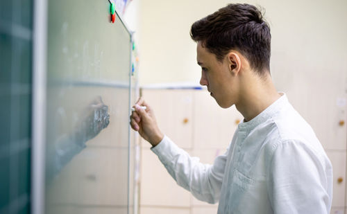 Side view of teenage boy writing on board with chalk