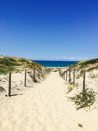 Walkway leading towards sea against clear blue sky on sunny day