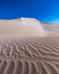 Sand dunes in desert against clear blue sky