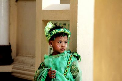 Boy in green costume looking away white standing against wall