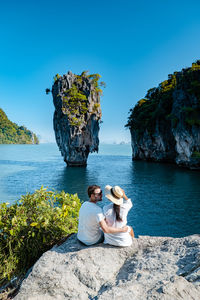 People sitting on rock by sea against sky