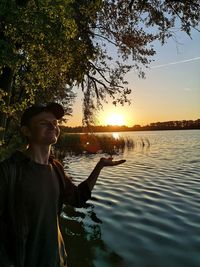 Man standing by lake against sky during sunset