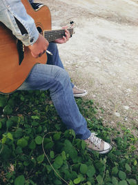 Low section of man playing guitar on field