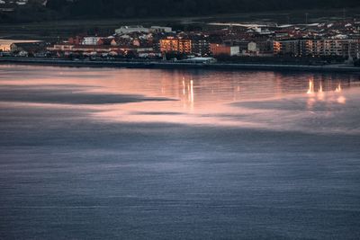 Illuminated buildings by sea against sky at night