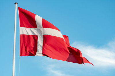 Beautiful flag of denmark or danish flag under the sun on a flagpole with blue sky on background