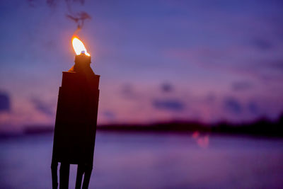 Close-up of illuminated candle against sky during sunset