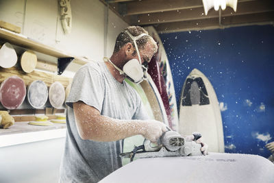 Man using plane on surfboard in workshop