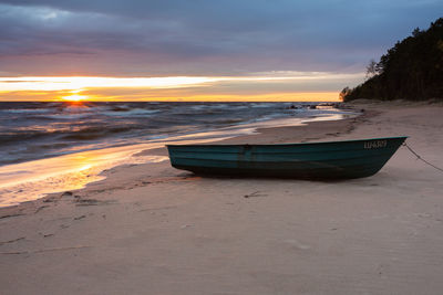 Boat moored on beach against sky during sunset