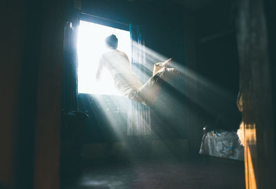 Man in mid-air by brightly lit window at home