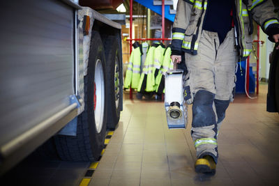 Low section of firefighter holding fire hose while walking at fire station