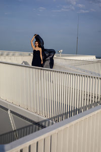 Woman standing on railing against sky