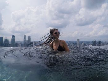 Woman splashing water in infinity pool against sky